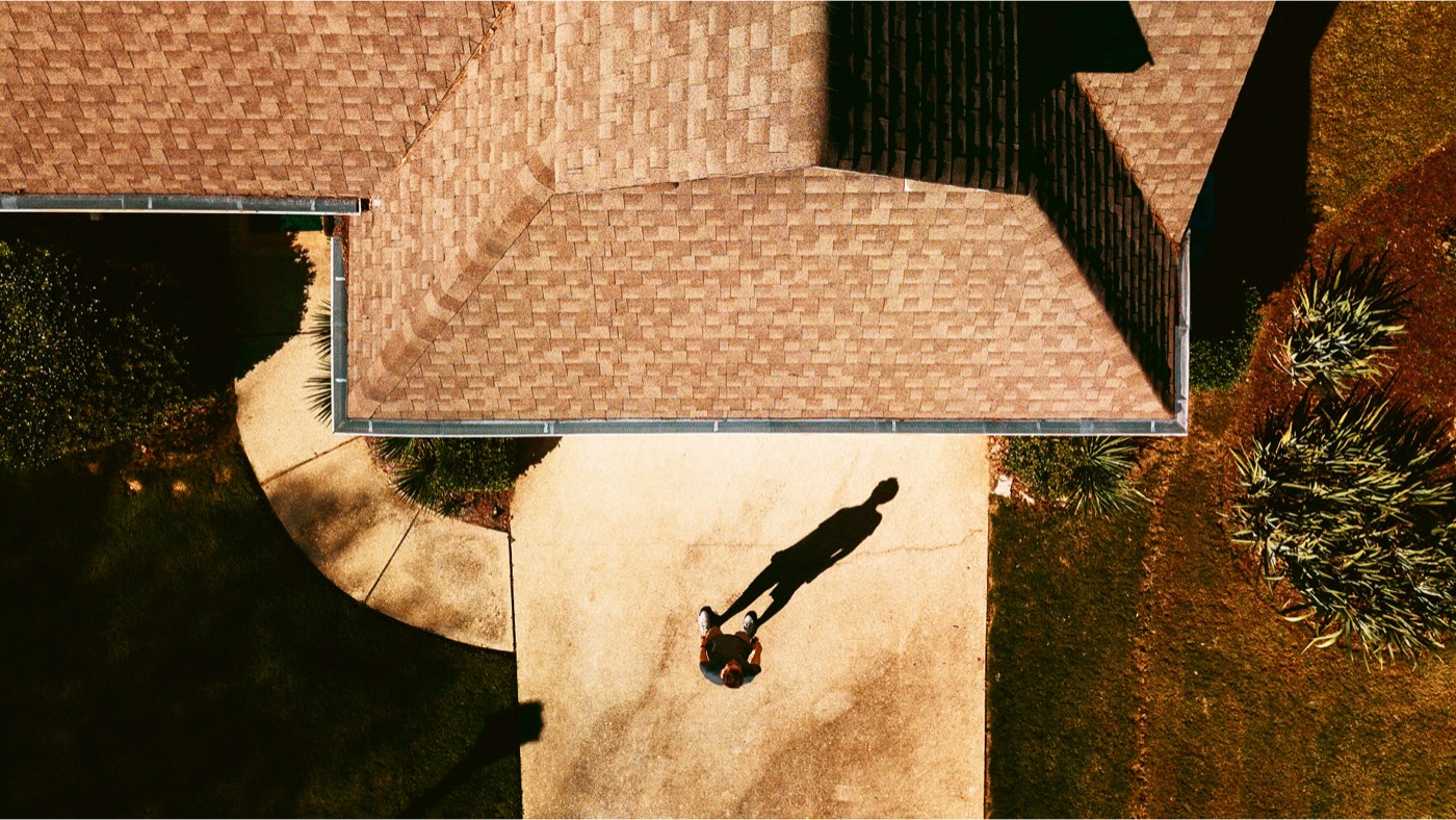 Aerial view of a shingle roof with a roofer's shadow on the driveway