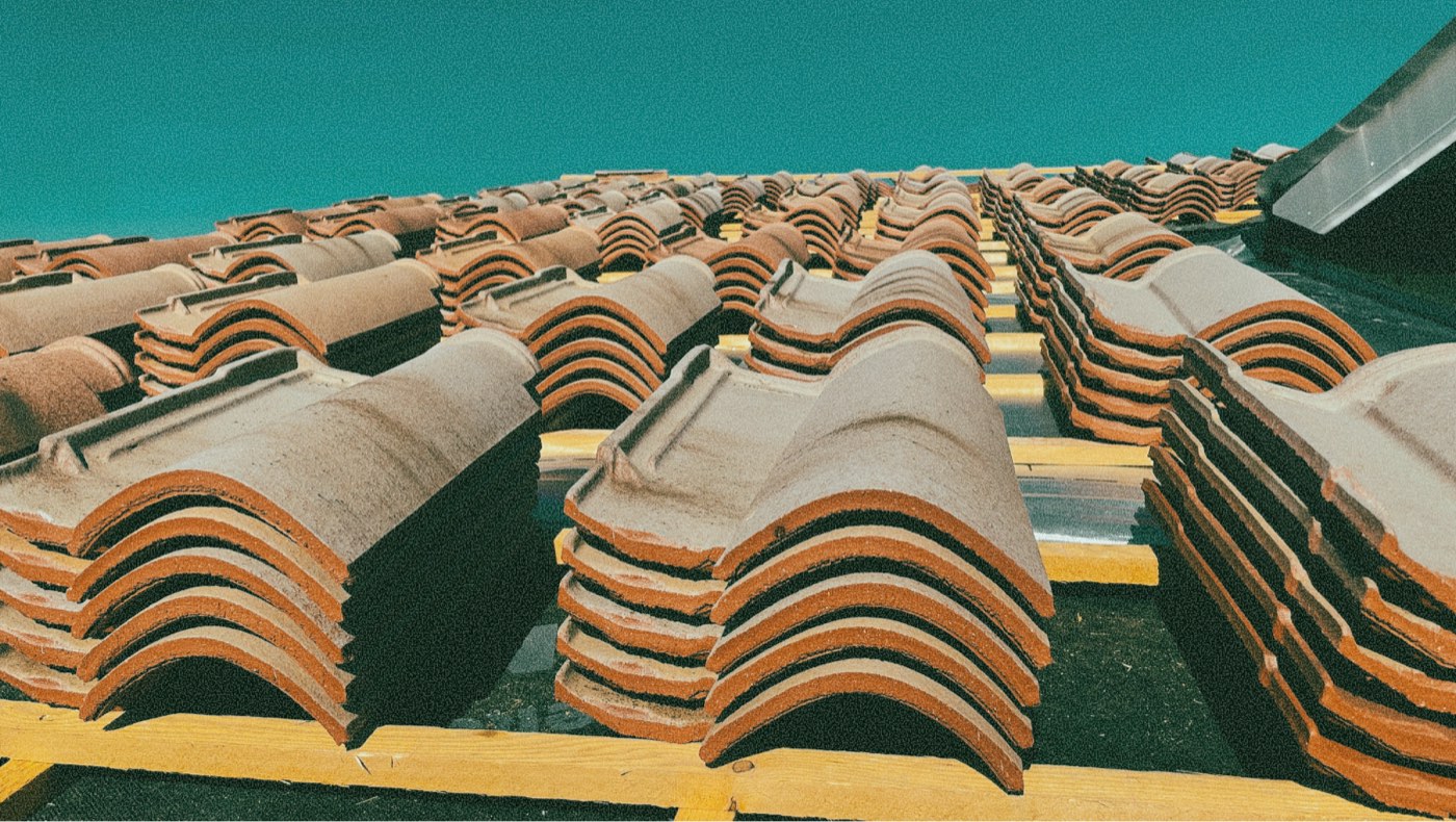 Stacks of clay roof tiles on battens under a clear sky